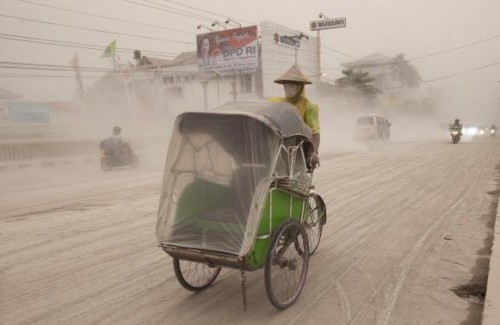 A man wears a mask as he rides a becak, a kind of rickshaw, on a road covered with from Mount Kelud,  in Yogyakarta