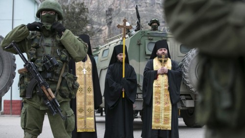 Orthodox monks pray next to armed servicemen near Russian army vehicles outside a Ukrainian border guard post in the Crimean town of Balaclava