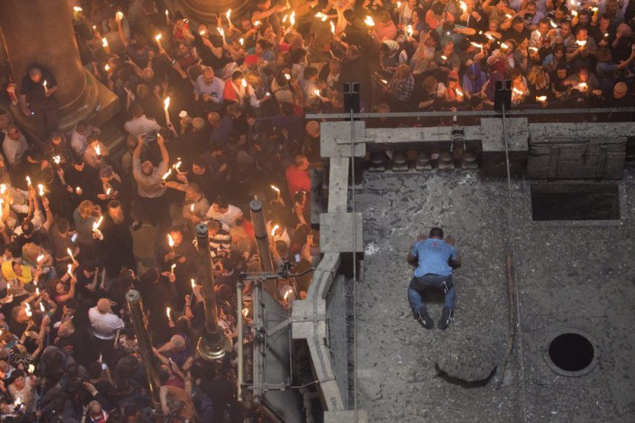 epa05284066 An Orthodox Christian worshipper on the roof of the Tomb of Christ as the miracle of the Holy Fire occurs in the Church of the Holy Sepulchre, Jerusalem, Israel, 30 April 2016. Eastern Orthodox Christians believe the Holy Fire, which emenates from within the Tomb of Christ and quickly spreads around the church and outside to Jerusalem and even to foreign countries, represents the flame of the Resurrection power, as well as the fire of the Burning Bush of Mount Sinai. EPA/ABIR SULTAN